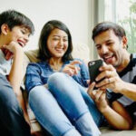A cool family laughs together as they look at photos on a smartphone, showcasing the fun of family group chats.