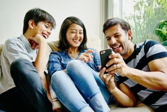 A cool family laughs together as they look at photos on a smartphone, showcasing the fun of family group chats.