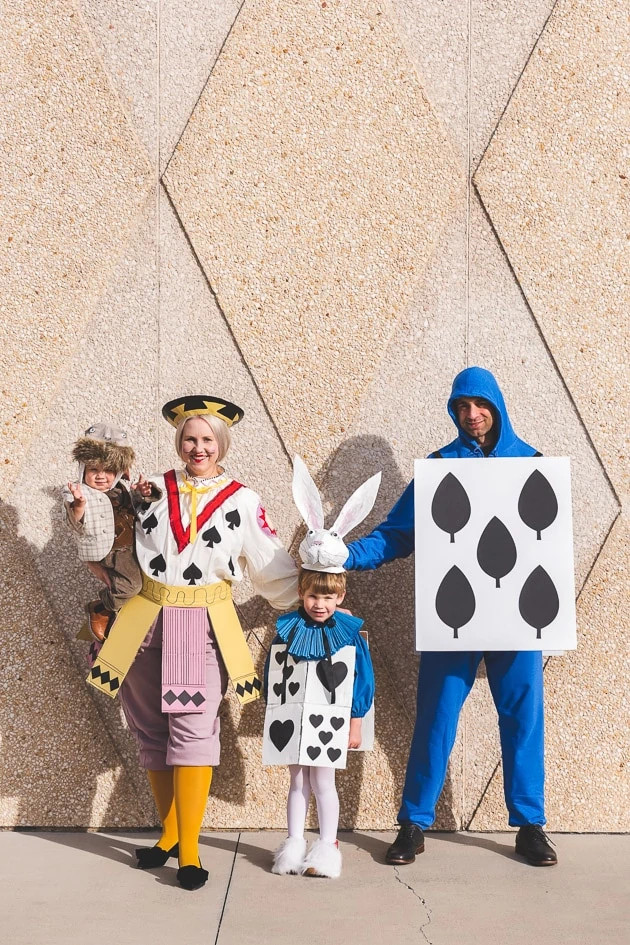 The whole family in their Alice in Wonderland costumes: walrus, rabbit, knight, and card man, posing together in a garden setting.