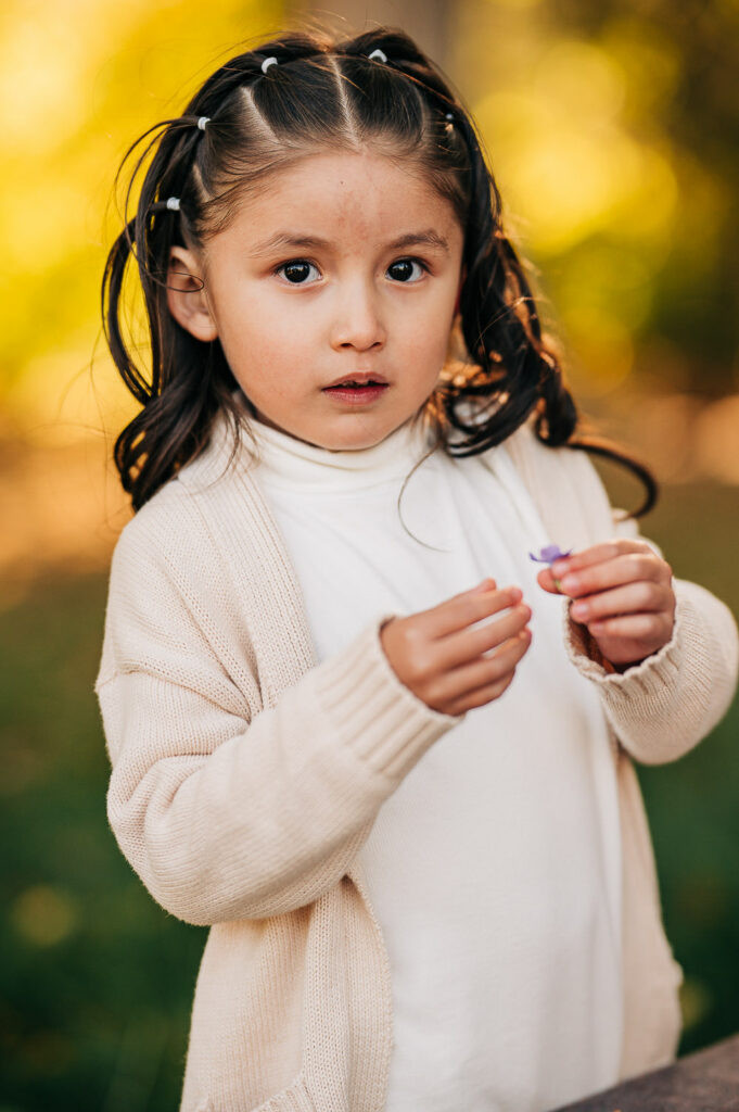 A toddler in a patterned dress and cardigan stands with her family, demonstrating layered and textured outfits for young children.