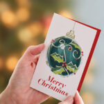 hands opening a christmas card with christmas tree in the background