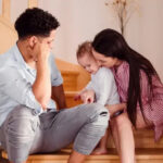 A young couple sits on the stairs and plays with their child. Securing your family's future with a family trust for generational wealth transfer.