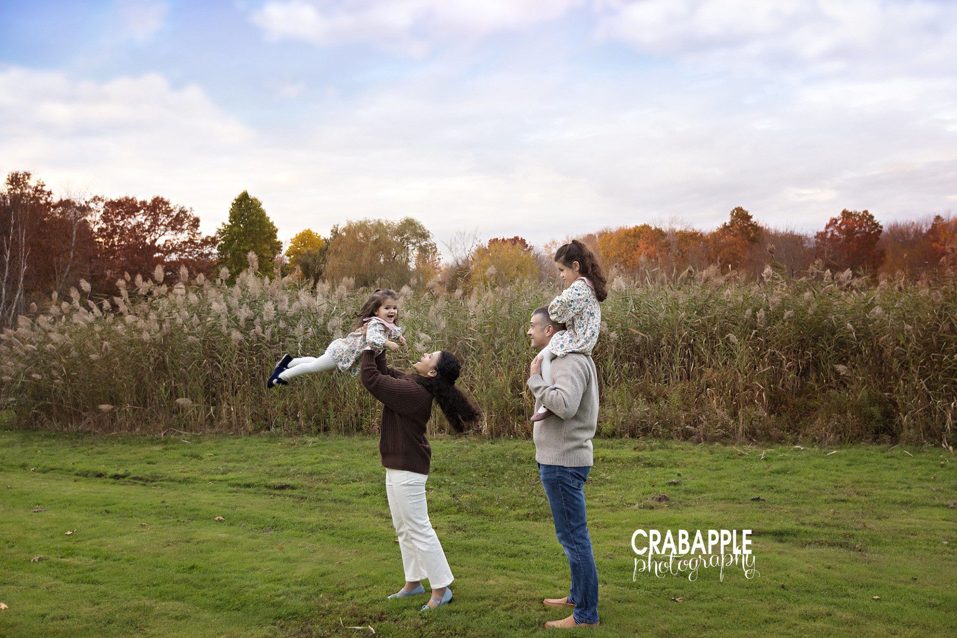 A family is photographed in a fun pose outdoors, showcasing playful interactions and candid moments during a family photoshoot.