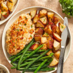 Parmesan baked chicken, roasted potatoes and green beans on white plate with fork and knife.