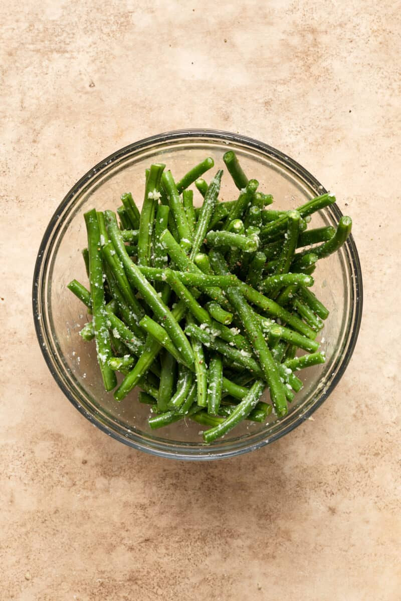 Green beans in bowl with seasoning and parmesan.