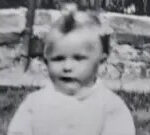 Susan as a baby wearing a white jumper and sitting on grass