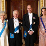 Queen Camilla, King Charles III, Prince William, and Catherine, Princess of Wales posing together in Buckingham Palace. Camilla is standing to the left of Charles, William is standing to the left of Kate.