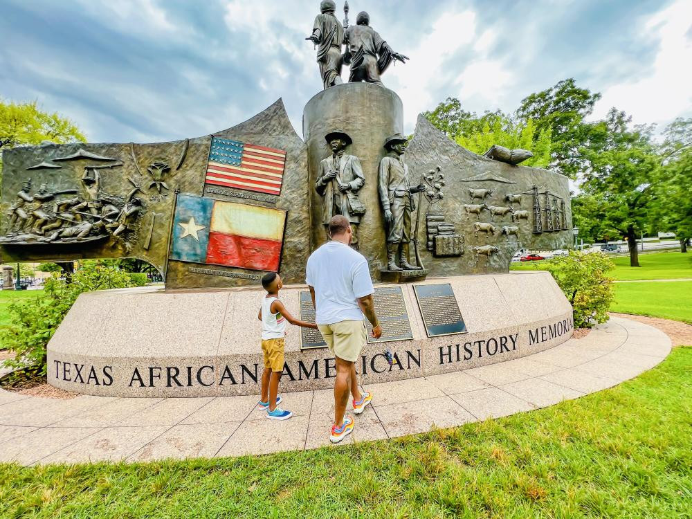 A father and son walk together in front of the Texas African American History Memorial at the Texas State Capitol, showcasing Austin family things to do