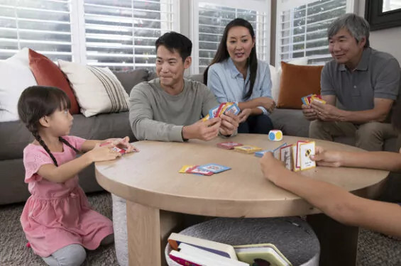 A family of four laughing while playing a board game at a table.